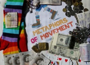 A variety of currencies, playing cards, colourful socks, jewellery, and confetti arranged around a Metaphors of Movement booklet illustrate vibrant financial metaphors in everyday life. | Andrew T. Austin | Metaphors of Movement