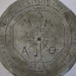 An antique circular stone or metal disc, engraved with various symbols, arrows, letters, and an outer ring of text in an unfamiliar script—known as the La Divinae Motum Orbis. | Andrew T. Austin | Metaphors of Movement