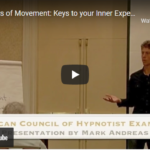 A man stands speaking in front of an audience, with a flip chart labelled Metaphors of Movement, sharing insights on self-discovery. A YouTube video title overlay appears at the bottom. | Andrew T. Austin | Metaphors of Movement