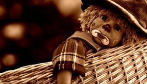 Sepia-toned photo of a sad clown doll with a dummy, curly hair, and checked outfit, resting against a woven basket—a whimsical reminder that even staff development and training can benefit from moments of reflection. | Andrew T. Austin | Metaphors of Movement